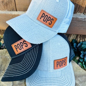 May include: Three gray and black baseball caps with a brown leather patch that says "POPS" on each cap.