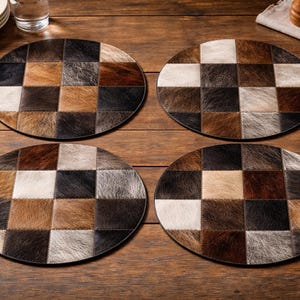 May include: Four round placemats with a patchwork design. Each placemat features a checkerboard pattern of various shades of brown, black, and white, creating a rustic and textured appearance. The placemats are set on a wooden table.