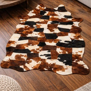May include: A patchwork cowhide rug in shades of brown, black, and cream. The rug has an irregular shape and is made of various geometric pieces. The rug is placed on a hardwood floor, adding a rustic touch to the room.