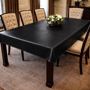 May include: A black leather dining table with a rectangular shape, surrounded by six upholstered chairs. A silver bowl with white flowers is the centerpiece. The table has dark brown legs and is on a neutral rug.
