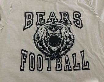 May include: A white t-shirt with a black graphic print of a bear with the words "BEARS FOOTBALL" in a bold, blocky font.