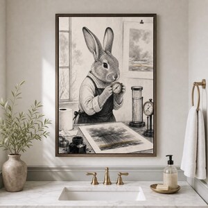 May include: A framed black and white wall art print depicting a rabbit wearing an apron, holding a small compass. The rabbit stands at a desk with a roll of paper, a glass cylinder, a small clock, and a drawing of a rainstorm on the table.