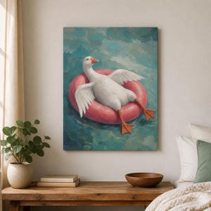 Puede incluir: Una impresión de arte mural con una pintura al óleo de un ganso blanco con pico naranja flotando en un flotador circular de color rosa brillante. El ganso está situado en el centro, rodeado de pinceladas texturizadas en tonos azul y cerceta.