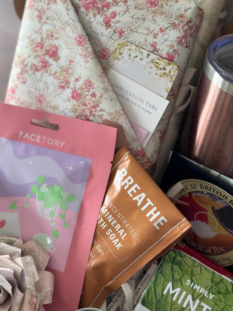 Close-up of blind date with a book box showing wrapped floral book, annotation tabs, tumbler, tea, and self care items. Mother’s Day gift for mom, cozy reading care package, and book lover gift set. Mystery book bundle designed for relaxing reading experiences, aesthetic bookish gifts, and thoughtful personalized book box ideas.