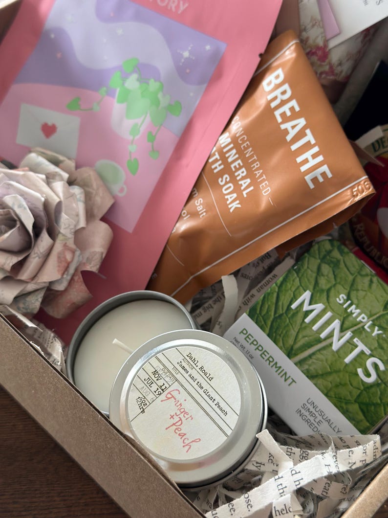 Close-up of Mother’s Day book box with candle, bath soak, tea, mints, and wrapped book arranged inside a curated blind date with a book gift set. Cozy self care box for readers featuring bookish accessories and relaxing essentials. Perfect gift for mom, book lover gift, mystery book bundle, and aesthetic reading care package for quiet nights and thoughtful gifting.