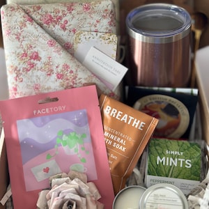 Mother’s Day blind date with a book box featuring wrapped floral book, candle, bath soak, face mask, tea, mints, and insulated tumbler arranged in a cozy self care gift set. Aesthetic book lover gift for mom, mystery book box idea, reader care package, and relaxing reading night essentials. Perfect book club gift, personalized book bundle, and thoughtful self care box designed for women who enjoy cozy reading experiences. Curated Book Box, Book Mail