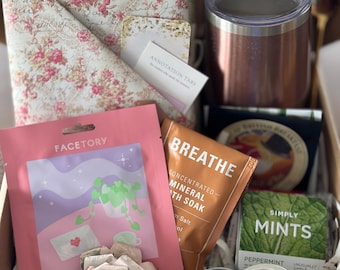 May include: A gift box containing a rose-patterned book cover, a rose gold tumbler, a pink Facetory sheet mask, a copper-colored Breathe mineral bath soak pouch, a Simply Mints peppermint box, a small candle tin, and a paper flower decoration.