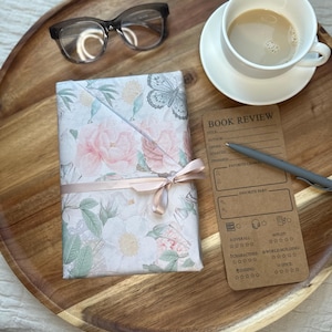 Cozy reading setup featuring wrapped floral book, coffee cup, glasses, and book review card on wooden tray. Mother’s Day book lover gift idea and blind date with a book concept showing relaxing reading moment. Perfect reader gift set, cozy self care experience, and aesthetic bookish gift for mom, book club members, and women who enjoy quiet reading time.