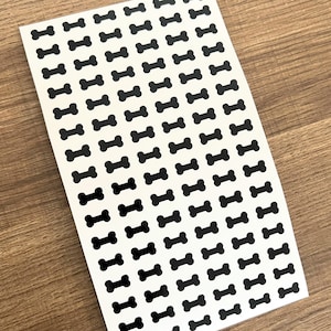 May include: A sheet of white paper with a repeating pattern of black bone-shaped stickers.