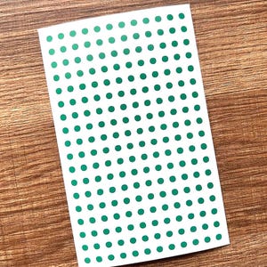 May include: A rectangular white sticker sheet featuring a grid of small, solid green circular adhesive dots arranged in uniform rows and columns across the entire surface of the paper, providing a simple and repetitive pattern for labeling.