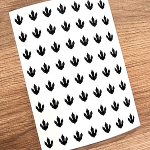 Könnte beinhalten: Ein Blatt weißes Papier mit einem sich wiederholenden Muster aus schwarzen Dinosaurierspuren.