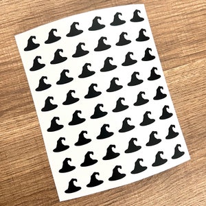 Pode incluir: Uma folha de papel adesivo branco com um padrão repetitivo de silhuetas de chapéus de bruxa pretos.