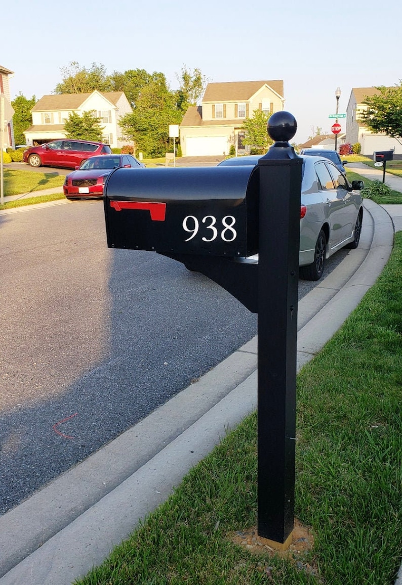May include: Black mailbox with a red flag and the number 938 on the front. The mailbox is mounted on a black post.