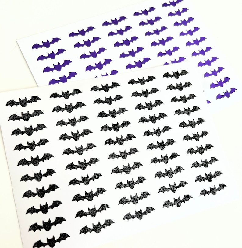 May include: Two sheets of white paper with black and purple glitter bats printed on them. The bats are arranged in rows and columns.