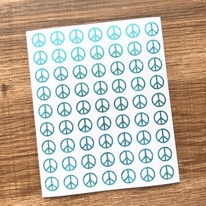 May include: A sheet of white stickers featuring a repeating pattern of teal peace symbols. The peace signs have a glittery texture, and are arranged in neat rows and columns. The stickers are on a wooden surface.