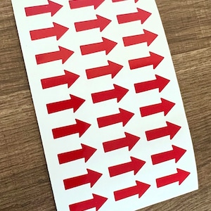 May include: A sheet of white paper with 25 red arrow stickers. The arrows point to the right.