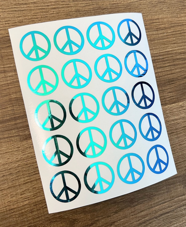 May include: A sheet of 20 peace sign stickers with a holographic finish. The stickers are iridescent blue and green.