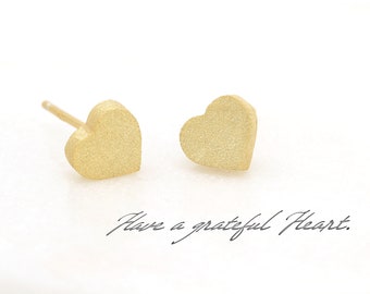 May include: A pair of gold heart-shaped stud earrings. The earrings have a brushed finish.