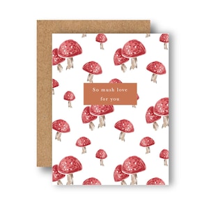 Pode incluir: Cartão de felicitações com fundo branco coberto por ilustrações de cogumelos vermelhos. O cartão apresenta um rótulo retangular castanho com o texto "So mush love for you". O cartão é combinado com um envelope castanho.