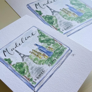 May include: Watercolor illustration of the book "Madeline" by Ludwig Bemelmans. The cover art features the Eiffel Tower, a group of girls, and a blue-robed figure. The title is written in cursive script. The artwork is on a white paper.