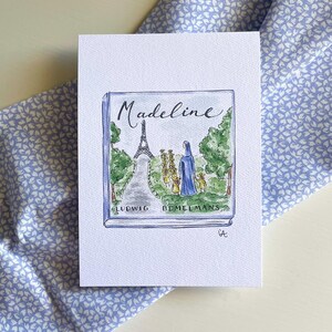 May include: A watercolor illustration of the book "Madeline" by Ludwig Bemelmans. The cover art depicts the Eiffel Tower and a group of girls in blue coats. The background is a light blue floral pattern.