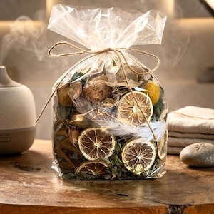 Könnte beinhalten: Ein klarer Zellophanbeutel, mit Bindfaden gebunden, gefüllt mit getrockneten Orangenscheiben, Blättern und Potpourri. Der Beutel steht auf einem Holztisch, mit einem Diffusor und Handtüchern im Hintergrund.