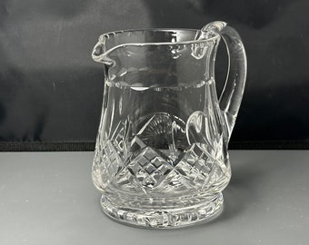 May include: A clear glass pitcher with a cut crystal design. The pitcher has a round body and a handle.