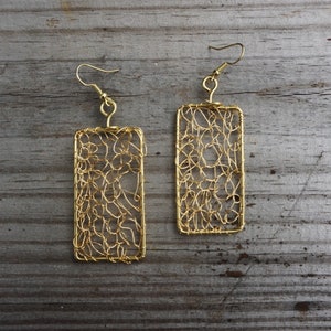 May include: A pair of gold wire earrings with a rectangular shape and a delicate, intricate design. The earrings are made of thin wire that is woven together to create a lacy pattern.