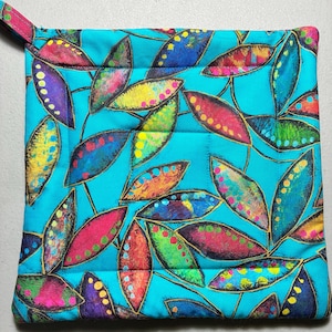 May include: A square quilted potholder featuring a vibrant turquoise background with a repeating pattern of stylized leaves in shades of magenta, yellow, green, blue, and purple, each outlined in black with small circular accents along the edges.