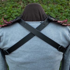 May include: A pair of red leather shoulder pads with black leather straps that cross in the back. The shoulder pads have a spiky design.