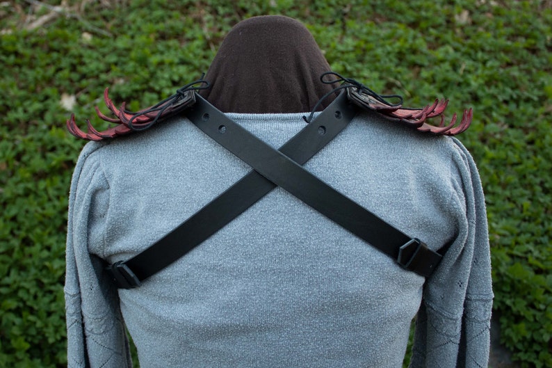 May include: A pair of red leather shoulder pads with black leather straps that cross in the back. The shoulder pads have a spiky design.