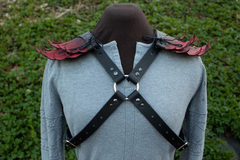 May include: Red leather shoulder armor with black straps and a silver ring. The armor is designed to look like wings with spikes.