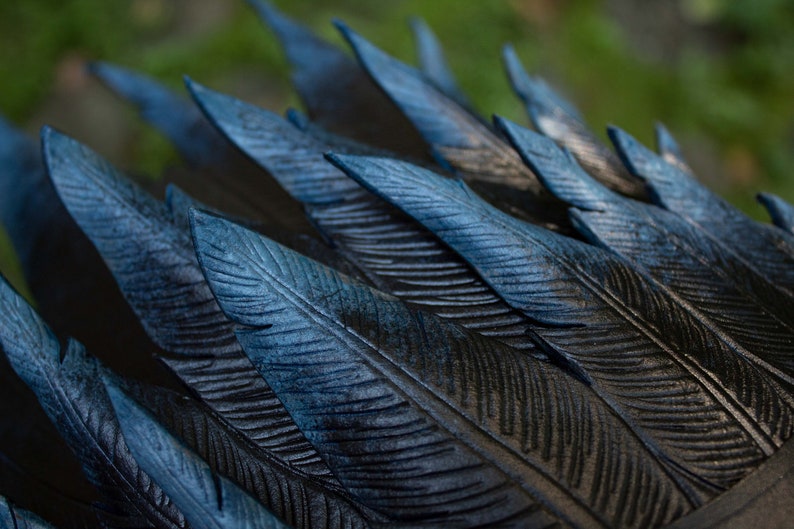 May include: Close-up of a dark blue and black carved wooden sculpture of feathers. The feathers are arranged in a fan shape and have a textured surface.