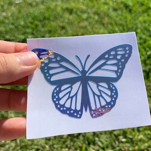 May include: A blue iridescent butterfly sticker on a white background.
