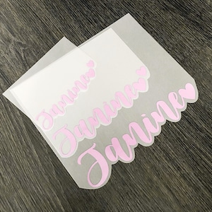 May include: Two sheets of clear transfer paper with the name "Jamirie" written in pink cursive letters with hearts.