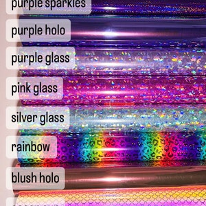 May include: A close-up of 12 rolls of vinyl adhesive with different colors and patterns. The colors include red, green, purple, pink, silver, rainbow, blush, ocean, gold, and gold. The patterns include sparkles, holo, glass, and a rainbow leopard print.