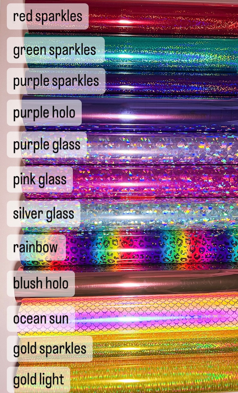 May include: A close-up of 12 rolls of vinyl adhesive with different colors and patterns. The colors include red, green, purple, pink, silver, rainbow, blush, ocean, gold, and gold. The patterns include sparkles, holo, glass, and a rainbow leopard print.