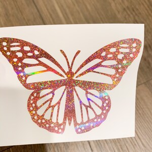 May include: A pink iridescent glitter butterfly decal. The butterfly has a detailed design with intricate wings.