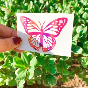 May include: A pink and purple butterfly sticker with white accents. The sticker is on a white background.
