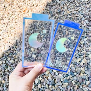 May include: Two clear plastic bookmarks with a blue border and a crescent moon and star design. The bookmarks have the text "dream daily" written on them.