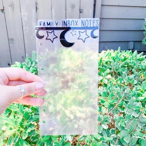 May include: A clear plastic sheet with holes punched along the left side. The sheet has a black header that reads "FAMILY INBOX NOTES" with a black crescent moon and star design.