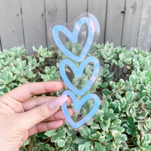 May include: Three blue heart-shaped stickers stacked on top of each other. The stickers are transparent and have a glossy finish.
