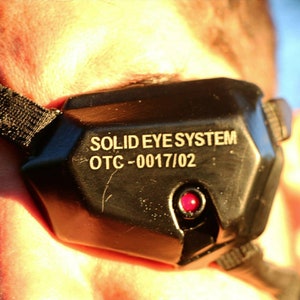 May include: A black device with a red light and the text "SOLID EYE SYSTEM OTC-0017/02" on it.