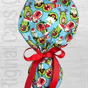 May include: A blue and green patterned scrub hat with a red ribbon tied around it. The pattern features avocados wearing Santa hats, reindeer antlers, and snowman scarves. The text "Merry 3" is printed below the hat.