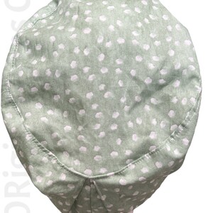 May include: A light green scrub cap with a white polka dot pattern. The cap is made of fabric and has a pleated design at the back. The cap is designed to be worn in a medical or professional setting.
