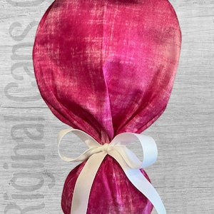 May include: A pink fabric pouch with a white ribbon tied around it. The pouch has a distressed, faded look.