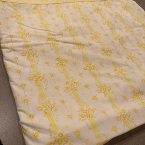 May include: A yellow and white striped fabric with a floral pattern. The fabric has a yellow border with white lace.