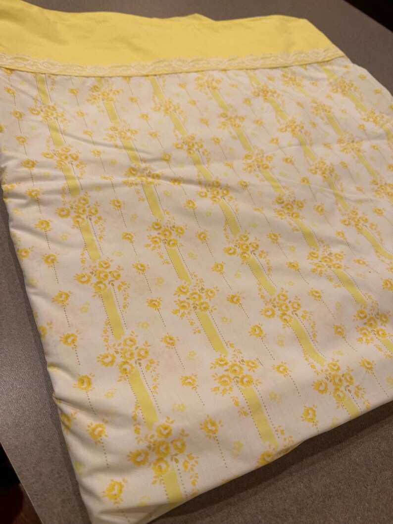 May include: A yellow and white striped fabric with a floral pattern. The fabric has a yellow border with white lace.