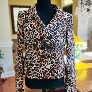 May include: A brown and black leopard print blazer with a double breasted closure and black buttons. The blazer is on a black mannequin.