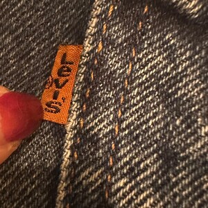 May include: Close-up of a dark blue denim fabric with a brown leather patch that says "Levi's" in white lettering.